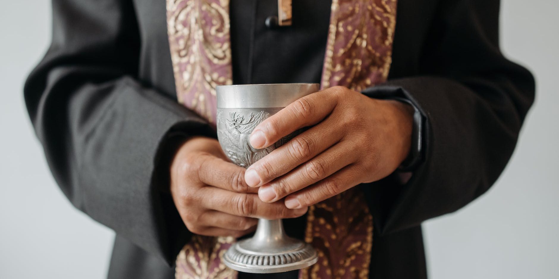 Padre visto do peito para baixo segurando uma taça de prata.